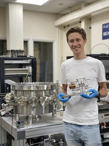 Jake Flowerdew, holding the previous IBEX Paul trap, stands next to the vacuum vessel containing the IBEX-2 trap in the IBEX lab at the Rutherford Appleton Laboratory.