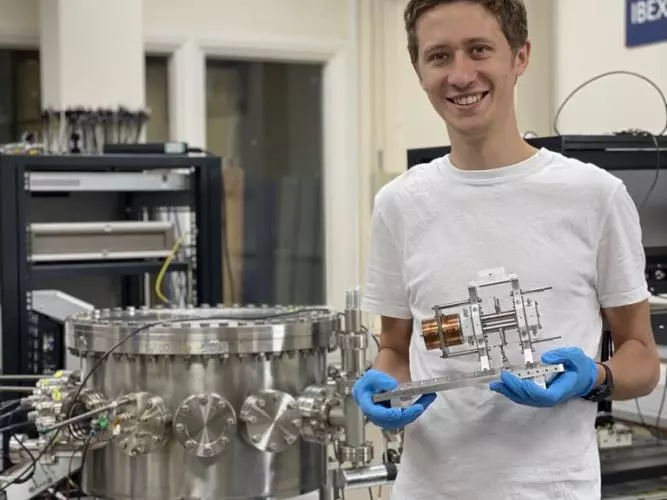 Jake Flowerdew, holding the previous IBEX Paul trap, stands next to the vacuum vessel containing the IBEX-2 trap in the IBEX lab at the Rutherford Appleton Laboratory.